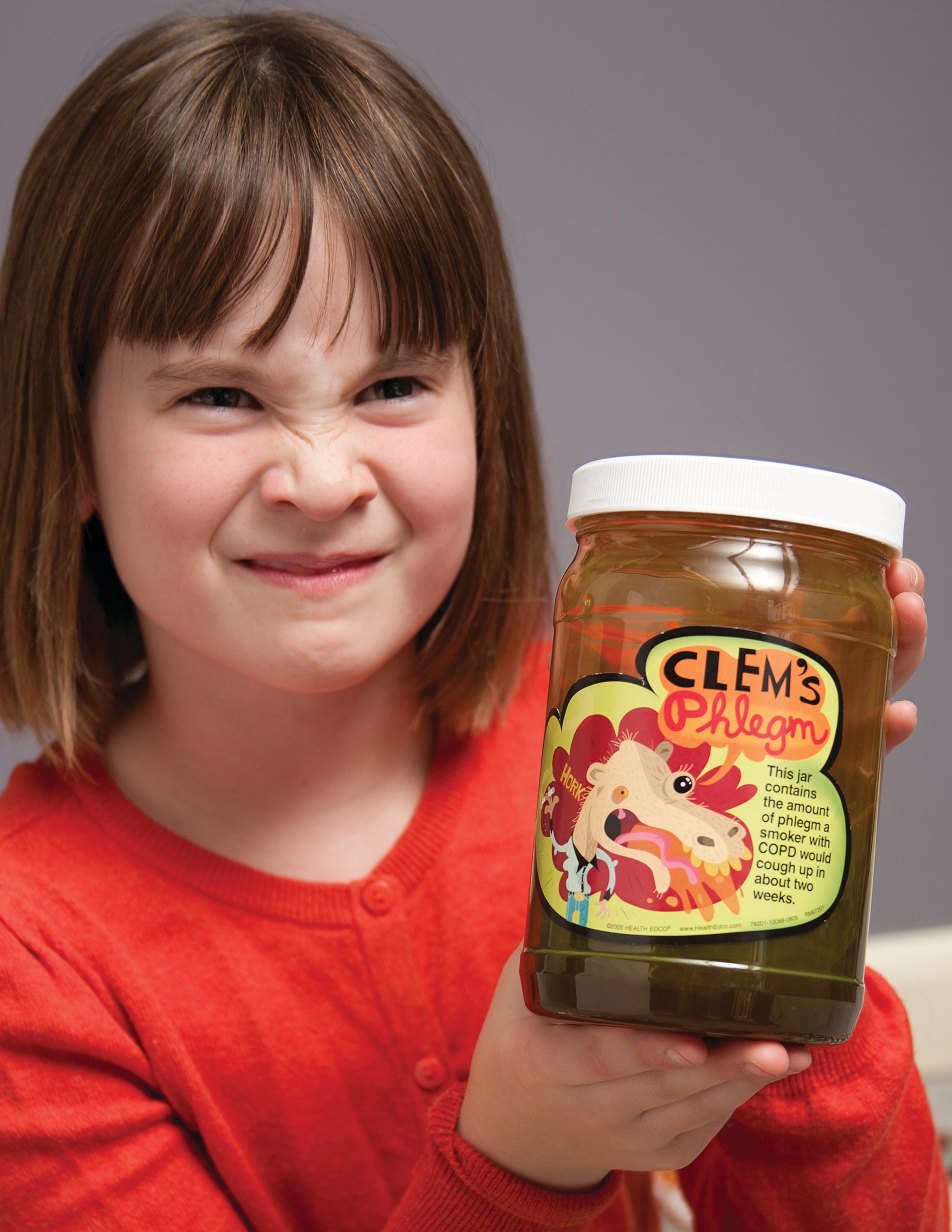 Little girl with a disgusted look on her face holding Health Edco’s Clem’s Phlegm Jar