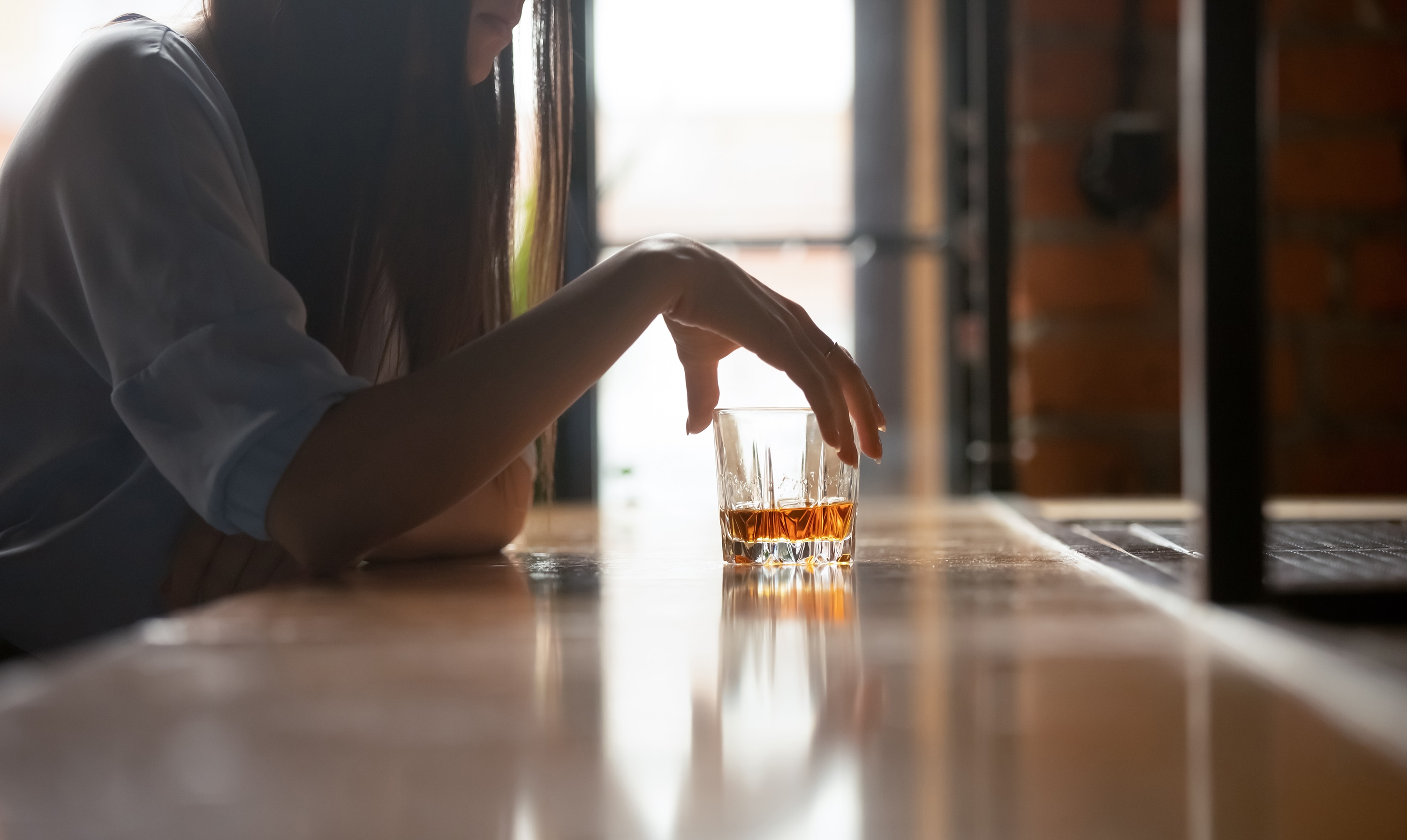 Depressed woman sitting alone at bar with whiskey